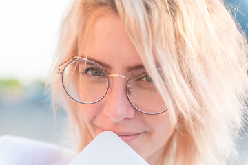 beautiful woman in round glasses in business clothes covers her face with a tablet. the sun shines brightly. close-up. horizontal photo