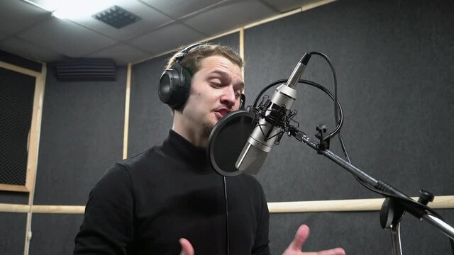 Voice actor in headphones on recording studio read a text near microphone to make a professional dubbing. Expressive scene of concentration near the microphone.