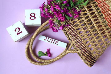 Calendar for June 28: cubes with the number 28 , the name of the month of June in English, a wicker basket and a bouquet of purple flowers, pastel background, top view