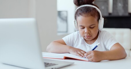 Afro american kid girl school pupil wearing headphones studying online from home watching web class lesson or listening tutor by video call elearning on pandemic isolation. Children remote education.