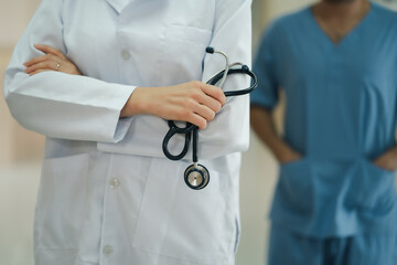 Close up shot hand of female doctor in white gown hold stethoscope with blur background of male nurse in blue uniform. Health care concept of hospital industry 
