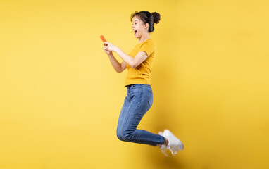 Fototapeta na wymiar Full body profile photo of young asian girl jumping high holding a phone writing a new social media post, isolated on blue background
