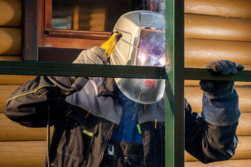 Close up of the a welder welds a fence on the construction site in the village. Construction on a metal frame.