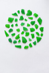 Round composition of various green assorted polished pieces of glass on a white background. Minimalistic natural background for invitation or greeting card with copy space.