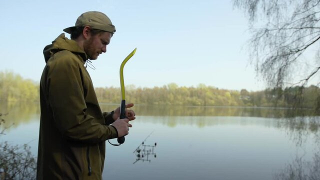 Fisherman baiting carp lake. Young caucasian male using bait thrower to add bait to carp fishing lake in uk. Shot at 200 fps slow motion.