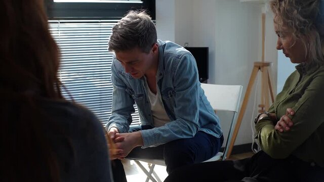 Tracking shot of desperate addicted alcoholic man share problem grief during interpersonal group therapy session. Depressed young male telling about mental problem to other patients near window.