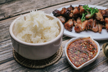 Grilled Pork Neck with Spicy sauce and steamed sticky rice on rustic wooden table, Thai Food.