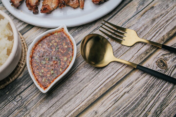 Grilled Pork Neck with Spicy sauce and steamed sticky rice on rustic wooden table, Thai Food.