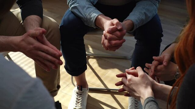 Close-up hands of unrecognizable multiethnic diverse men and women sitting in circle during group interpersonal therapy session. Tracking shot of people telling about his mental problem or addiction.