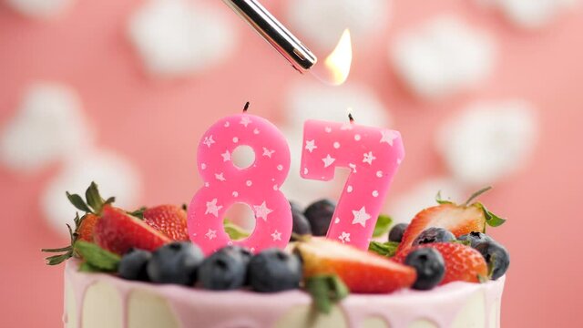 Birthday cake candle number 87. Candle and cake on pink background and fire by lighter. Close-up and slow motion
