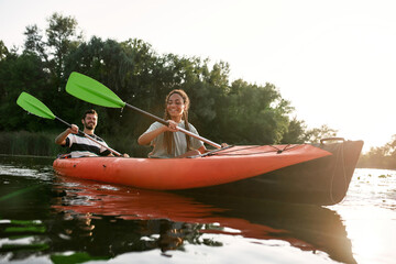 Smiling young woman and her boyfriend enjoying kayaking in a lake on a late summer afternoon