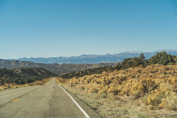 Two lane road in the arid Sierra Nevada's leading to mountains against blue sky