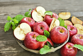 A lot of fresh Royal Red Gala apples with green leaf and water drop in basket on wooden background.