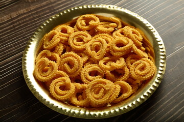 Indian snack foods- delicious crispy fried spicy chakli, chakkli, murukku served in brass plate.