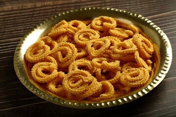 Indian snack foods- delicious crispy fried spicy chakli, chakkli, murukku served in brass plate.