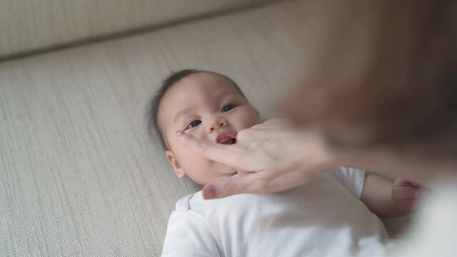 asian woman mother parent playing tickle with baby infant on sofa bed. close up happy laughing face of kid being provoke. mom using fingers tickling kid big smile and funny.