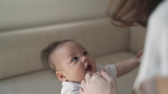 mother woman assist pull up asian baby infant to sit and play. baby put effort learning skill development muscle. kid holding parent hand trying to balance body.