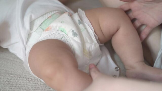 mother woman hand release button on baby infant clothes jumper. closeup parent take off baby clothes before bath and changing diaper.