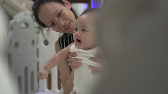 asian baby infant learning walking skill development by mother woman encourage at home. parent mother assist helping baby standing lesson. authentic life at home. baby infant playing in playpen. stand