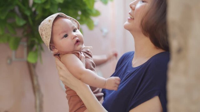 asian woman mother holding baby infant playing and kiss indoor. happy baby infant in hat jumping. mom play with daughter happily.