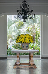 grand entrance with marble table, asian ceramic vase and large yellow floral arrangement and beautiful palms, chandelier and architectural features. interior and exterior