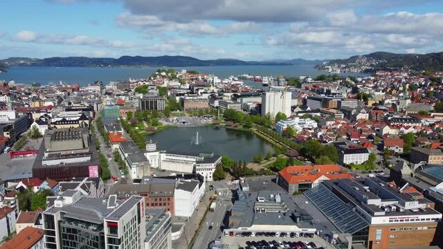 Forward moving aerial Bergen city centre with water fountain in park and seafront in the background - Norway