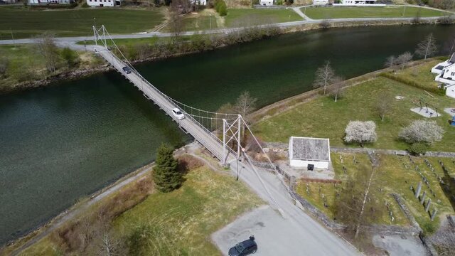 Two cars crossing over Modalen river on old suspension bridge - Aerial Modalen Norway with church