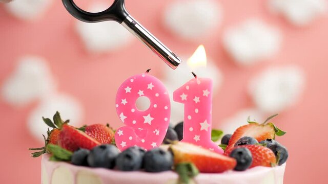 Birthday cake candle number 91. Candle and cake on pink background and fire by lighter. Close-up and slow motion