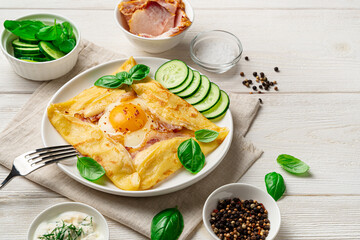 French pancake with egg, bacon and cheese on a white background.