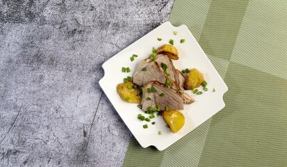 Oven baked pork shoulder with potatoes  on a white square  plate on a dark background. Top view, flat lay