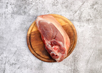 Raw pork shoulder on the skin with bone on a round wooden cutting board on a dark grey background. Top view, flat lay