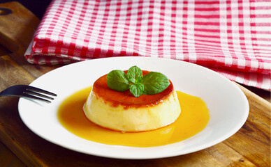 Caramel custard desert on white dish with wooden background.