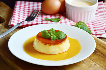 Caramel custard desert on white dish with wooden background.