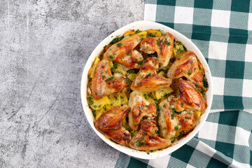 Oven baked chicken wings with potatoes in a white baking dish on a dark grey background. Top view, flat lay