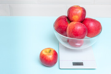 Red apples in a transparent bowl on a kitchen scale, copy space, close-up. The concept of healthy eating, losing weight, weight control. Healthy snack