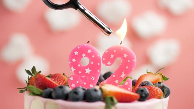 Birthday cake candle number 92. Candle and cake on pink background and fire by lighter. Close-up and slow motion