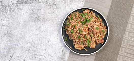 Buckwheat pilaf with meat on a round plate on a dark grey background. Top view, flat lay