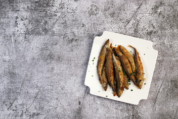 Pan fried capelin or smelt fish on a white square  plate on a dark background. Top view, flat lay
