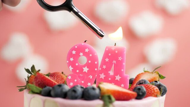 Birthday cake candle number 94. Candle and cake on pink background and fire by lighter. Close-up and slow motion