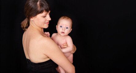 Happy mother kissing baby boy. Mother caring after her babys skin. Sensual mom and baby hugging. Mother holding beautiful baby son. Tenderness. Beautiful image of maternity. Studio shot. Babycare