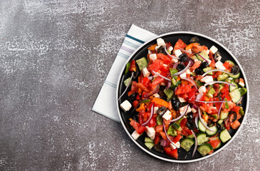Greek salad with olives, tomatoes, cucumbers, pink onions and feta cheese on a round plate on a dark background. Top view, flat lay.