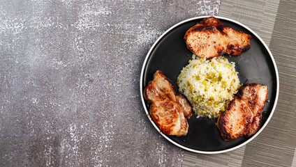 Pork loin with rice on a round plate on a dark background. Top view, flat lay