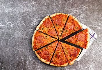 Pizza with pepperoni and olives on a round wooden cutting board on a dark background. Top view, flat lay