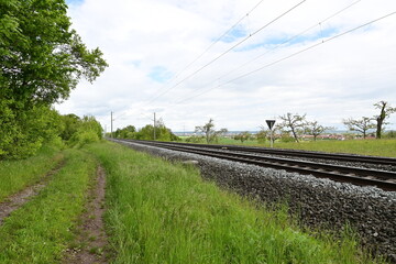 Fototapeta na wymiar Railway line with 2 railway tracks and rails next to a dirt road near Bergrheinfeld, Schweinfurt, Bavaria, Germany