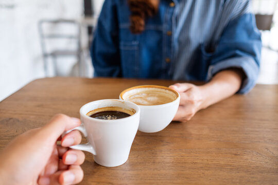 Closeup image of a woman and a man clinking coffee cups together in cafe
