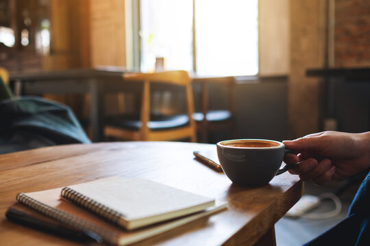 Closeup image of a woman holding coffee cup with notebooks on wooden table