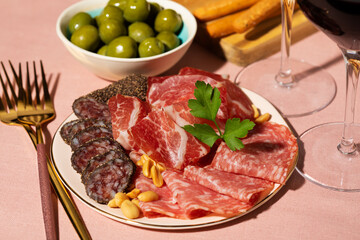 Two glasses of red wine, charcuterie and olives on pink background