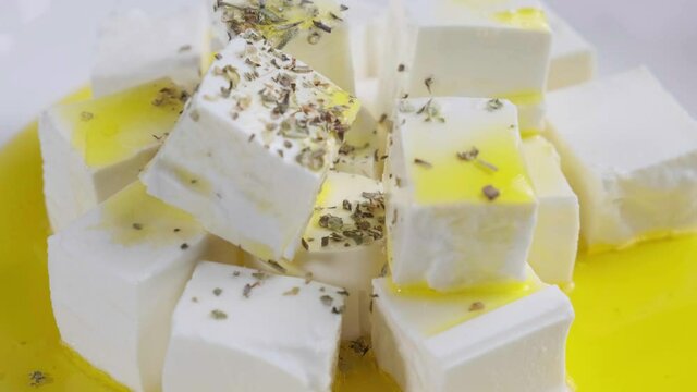 Feta cheese with olive oil and dried herbs on a white plate.