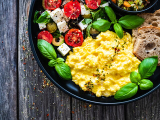 Continental breakfast - scrambled eggs, bread and greek salad on wooden table
