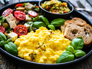 Continental breakfast - scrambled eggs, bread and greek salad on wooden table
